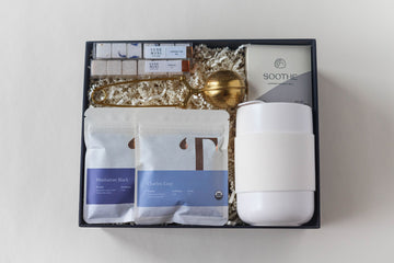 tea gift box featuring lavender bath bomb, luxe mini sugar cubes in vanilla and London fog flavors, 2 tea tasting packets - Charles grey and Manhattan black, ceramic portable mug in cream and a gold tea strainer.