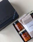 Bath salts, coconut milk bath, 2 pairs of cozy socks, massage candle and card game for couples in a black gift box with lid displayed off to the side.