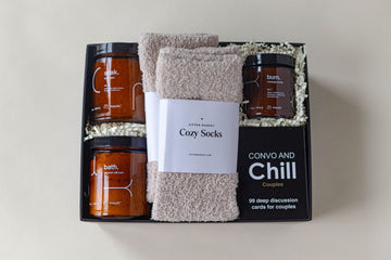 Bath salts, coconut milk bath, 2 pairs of cozy socks, massage candle and card game for couples in a black gift box. 